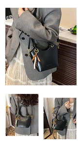 Detail of black leather bucket bag with ethnic beaded charm and adjustable strap