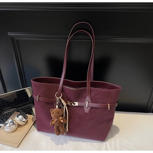 Detail view of burgundy tote bag showing matte texture and golden buckle with bear charm