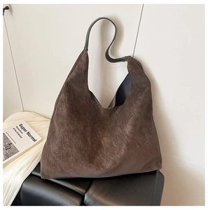 Detail of a minimalist dark brown suede hobo tote bag placed on a black leather bench