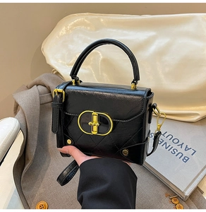 Close-up of black leather crossbody bag with golden oval buckle and quilted pattern detail