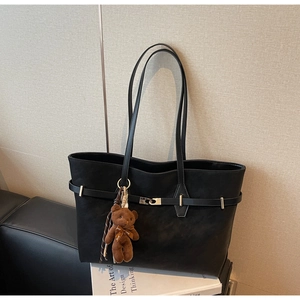 Detail of black leather tote bag with metal buckle and teddy bear charm on sofa