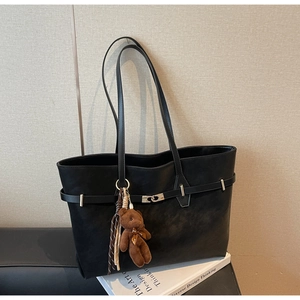 Detail of black tote bag with silver buckle strap, plush bear charm and striped tassel