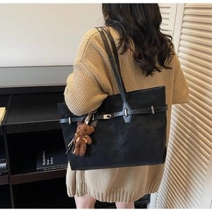 Detail of black suede tote bag with brown teddy bear charm on beige knit sweater