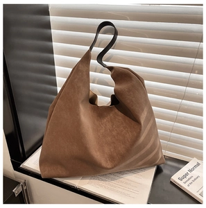 Macro detail of caramel brown suede tote bag with black leather handle in soft window light