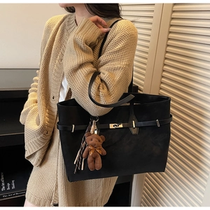 Close-up of black suede tote bag featuring a leather belt buckle and cute bear charm