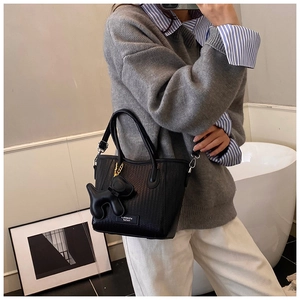 Detail of black woven texture tote bag featuring a cute dog charm and metallic brand plaque