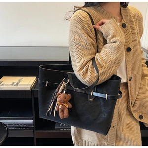 Detail of black matte tote bag with gold buckle and cute brown bear plush pendant
