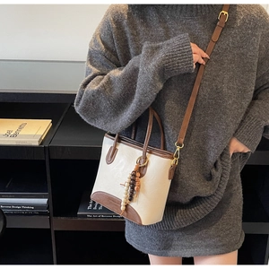Detail of a two-tone mini crossbody bucket bag featuring a decorative wooden bead tassel