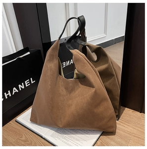 Detail of vintage brown suede tote bag with black handles on a wooden floor