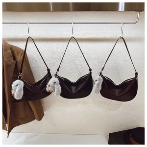 Detailed view of three black crescent shoulder bags with plush rabbit charms hanging on hooks