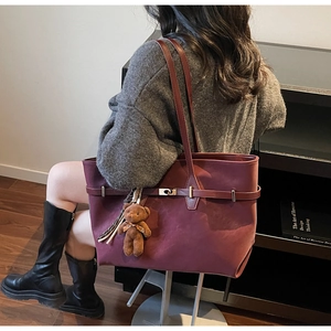 Detail view of burgundy tote bag with gold buckle and brown plush bear charm