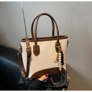 Detail of a two-tone beige and brown leather tote bag with stylish beaded pendant charm