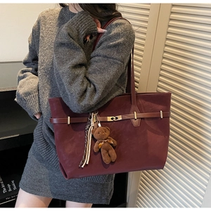 Detail of burgundy tote bag with gold buckle, plush bear charm and striped scarf decoration