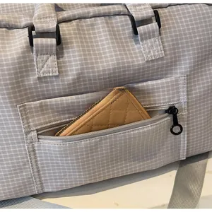 Detail der grauen Reisetasche mit Karomuster, Reißverschlusstasche und Schultergurt