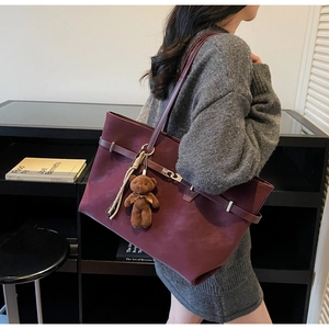Deep burgundy tote bag with silver buckle and plush bear charm shown in lifestyle setting