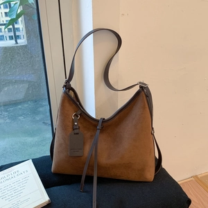 Detailed view of brown suede dumpling bag with tassel charm and leather shoulder strap