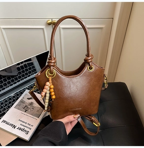 Detailed macro view of dark brown leather bucket bag with beaded charm and gold hardware