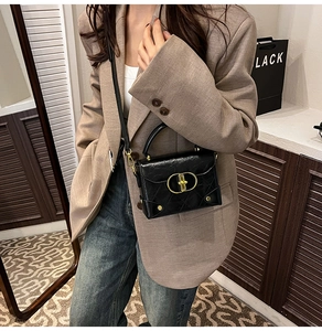 Crossbody bag in black glossy leather with gold ring clasp worn by model in suit