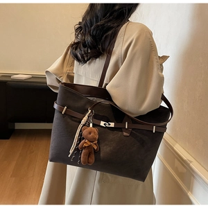 Detail view of large dark brown tote bag with suede texture and teddy bear charm on model