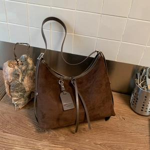 Detail of dark brown matte suede hobo bag with genuine leather tag and silver hardware