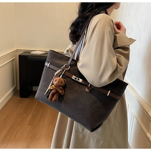 Detail of dark brown suede tote bag featuring silver metal lock and cute bear charm