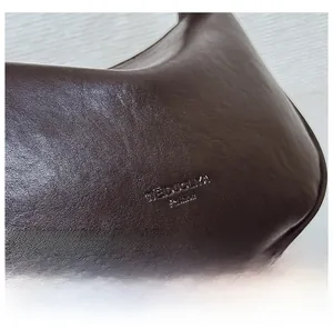 Detail shot of the dark brown lychee textured leather and embossed brand logo on the bag