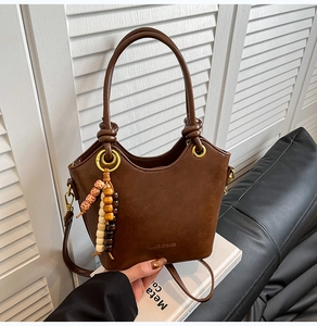 Detail of a brown leather bucket bag with gold hardware and a colorful wooden bead charm
