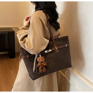 Detail of dark brown tote bag with bear charm and buckle shown from a side view
