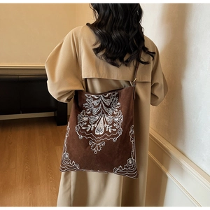 Detail der dunkelbraunen Wildleder-Tragetasche mit weißer Stickerei auf beigem Trenchcoat