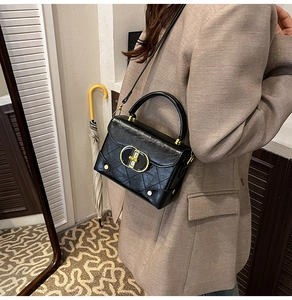 Detail of black quilted crossbody bag with golden clasp and studded corners on model