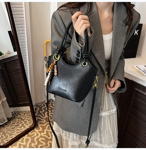 Close-up of black matte bucket bag with wood bead charm and soft leather texture
