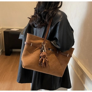 Detail of a brown suede tote bag featuring a leather strap and a cute teddy bear charm