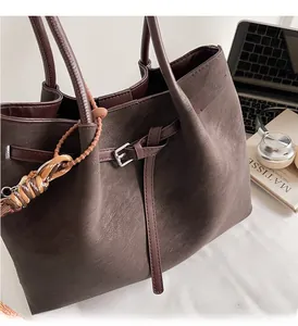 Detail of dark brown suede tote bag featuring silver metal buckle and woven strap ornament