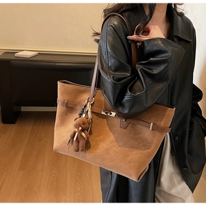 Close-up of brown tote bag with cute bear pendant and bow detail on leather strap