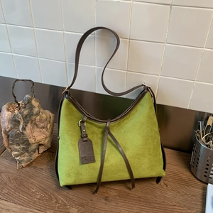 Detailed view of matte green suede bag with brown leather trim and brand logo tag