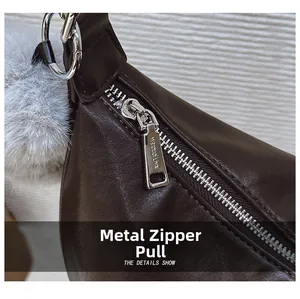 Close-up of silver metal zipper hardware and fluffy grey fur pompom on dark brown bag