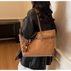 Close-up of a brown tote bag with decorative metal buckle and plush bear charm on a model