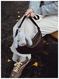 Close-up of dark brown leather hobo bag with cute plush rabbit charm and logo detail