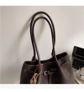 Detail of dark brown matte tote bag with thin straps and decorative braided charm accent