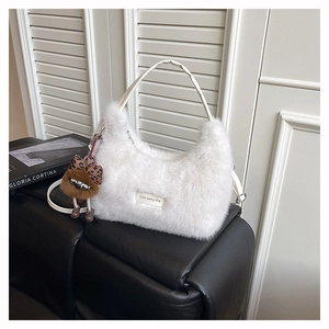Detail of white plush shoulder bag with leather strap and cute furry doll pendant