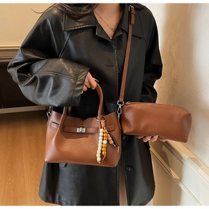 Gros plan d'un sac seau en cuir marron avec fermoir rotatif argenté et breloque perlée