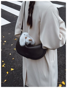 Detail of a black leather half-moon shoulder bag featuring a plush bunny charm on the strap