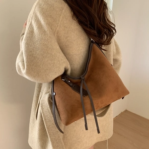 Brown frosted leather hobo bag with side straps worn by a model in a minimalist setting
