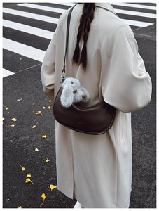 Detail of dark brown leather half-moon bag with cute plush rabbit charm on a street