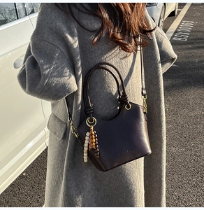 Detail of dark brown leather bucket bag with wooden bead charm and adjustable strap