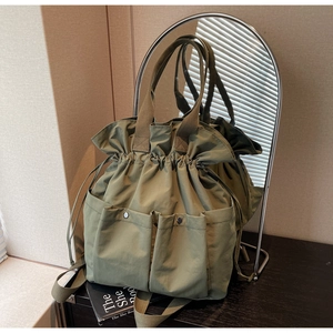 Detail of olive green drawstring bucket bag with side pockets on a wooden desk
