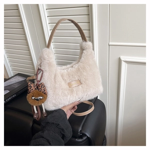 Detail of plush beige shoulder bag with brown leather handles and a cute bear charm