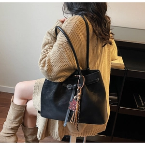 Detail view of black leather tote bag with unique leopard bear charm and tassel on side