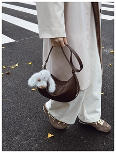 Detail of dark brown leather hobo bag with a plush bunny charm on a city street