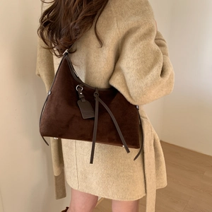 Detail of a dark brown suede crossbody bag with long strap on a beige coat